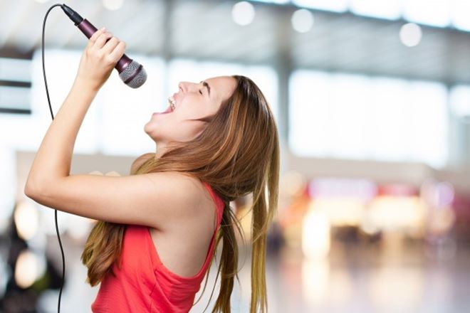 Jovem mulher cantando com um microfone no fundo branco — © Reprodução