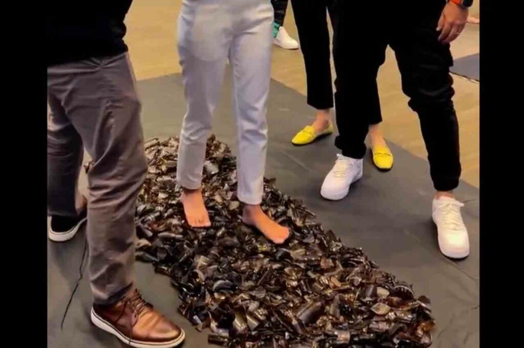 Mulher anda descalça sobre cacos de vidro durante dinâmica motivacional em evento com empresários