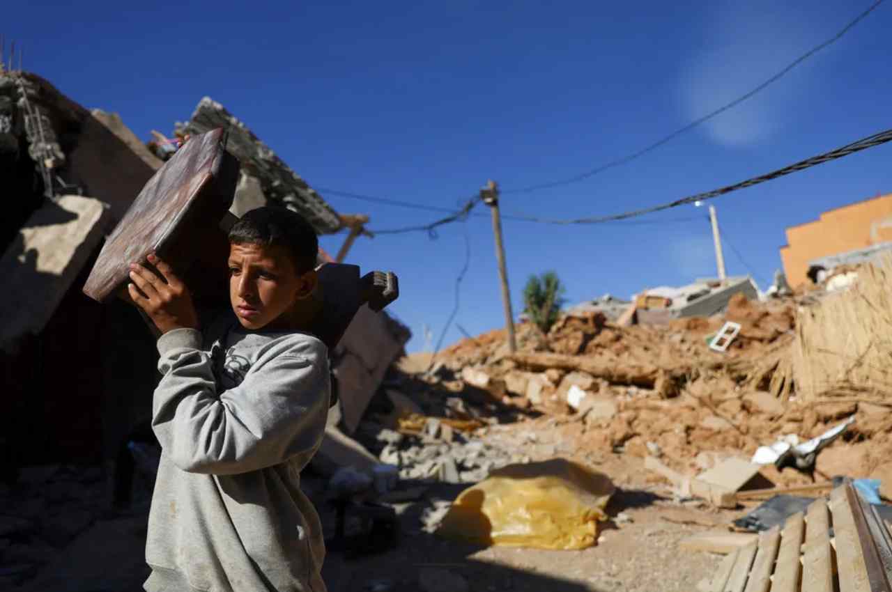 Menino carrega móvel em vilarejo destruído por terremoto no Marrocos | © Hannah McKay/Reuters