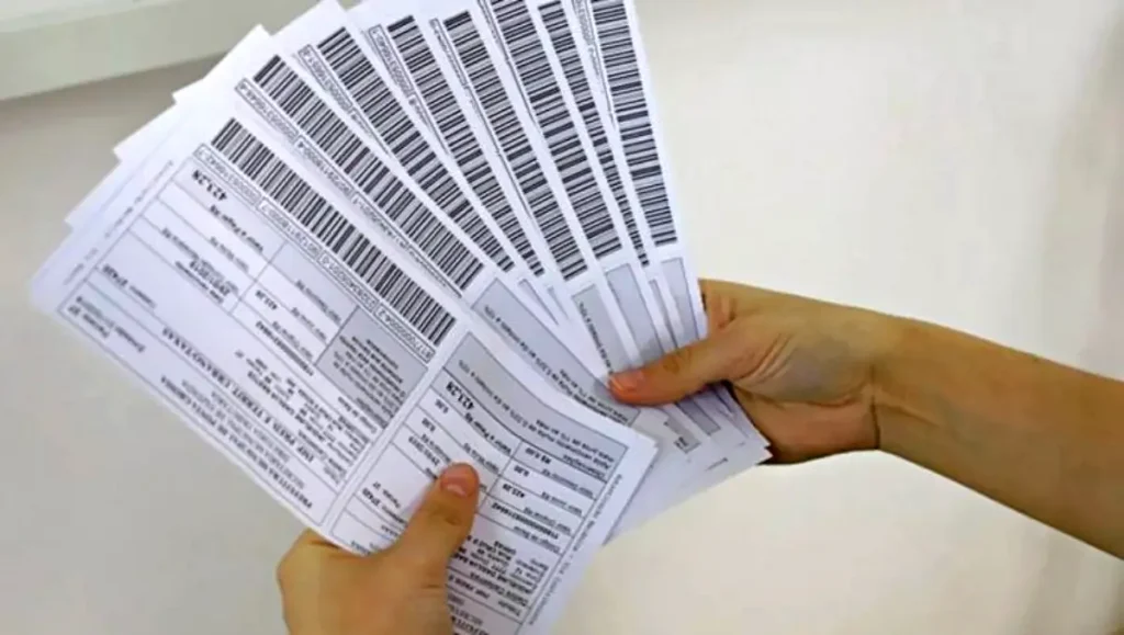 Pessoa segurando vários boletos de IPTU com códigos de barras para pagamento de imposto municipal