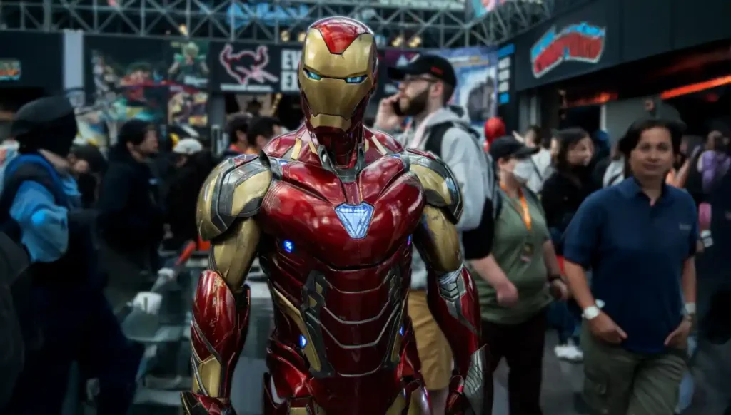 Cosplayer com armadura vermelha e dourada posa em evento de cultura pop com público ao fundo