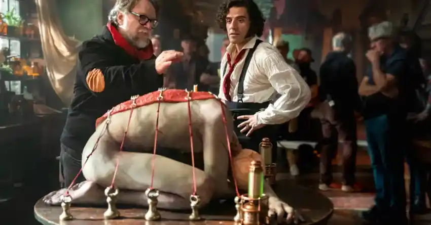 diretor orienta ator em cena do filme Frankenstein da Netflix com criatura deitada sobre mesa em set de filmagem