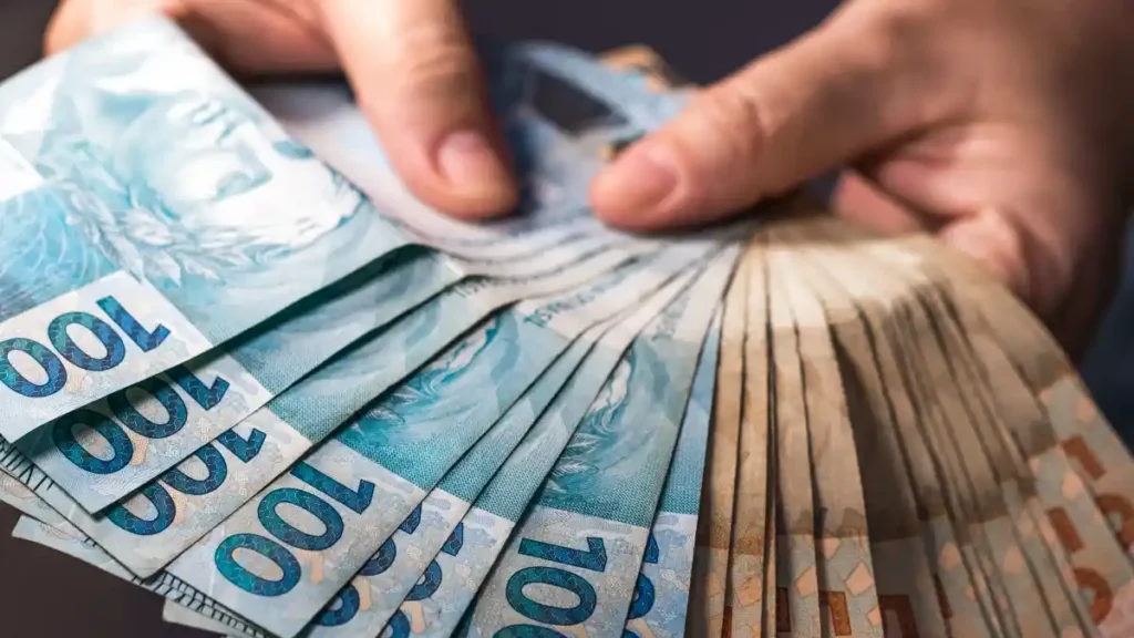 Mãos seguram notas de real brasileiro em leque, representando dinheiro em espécie