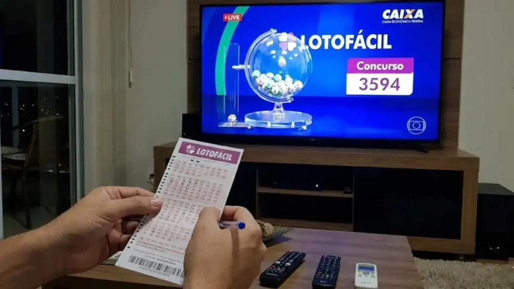 Apostador marca bilhete da Lotofácil enquanto assiste ao sorteio da Caixa na TV, com o concurso 3594 na tela