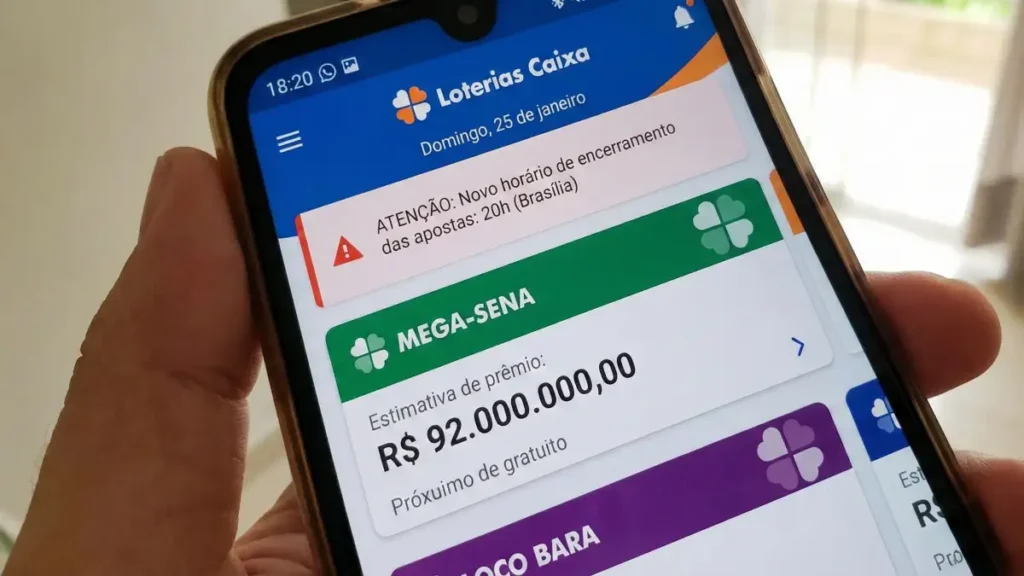 mão segura celular com aplicativo Loterias Caixa exibindo a Mega-Sena e estimativa de prêmio de 92 milhões de reais