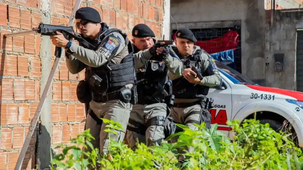 policiais da Força Tática realizam operação em área urbana com equipe armada e viatura ao fundo durante ação de segurança pública