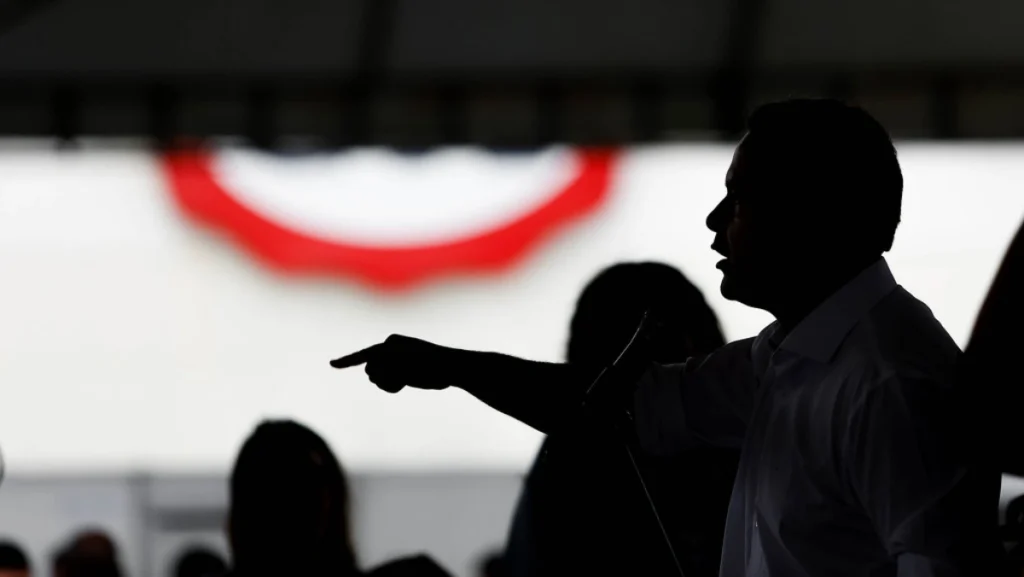 Renan Filho aparece em silhueta durante discurso em evento, apontando com a mão em cima do palco