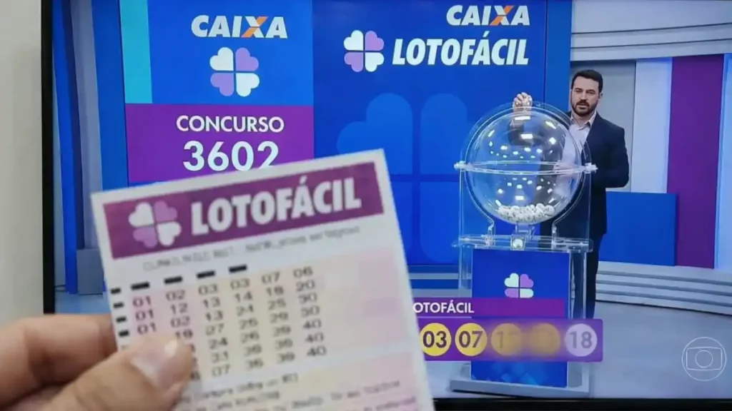 Volante da Lotofácil em primeiro plano com transmissão do sorteio da Caixa ao fundo exibindo concurso 3602 e números do resultado na tela