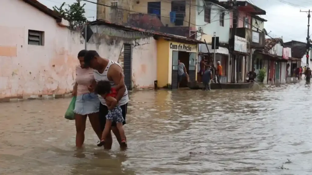 Família atravessa rua alagada após forte chuva em bairro urbano de Alagoas durante fim de semana com raios e trovoadas