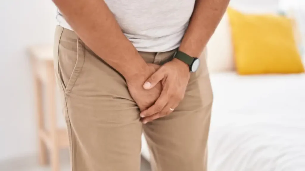 Homem com dor na região genital segurando a virilha dentro de um quarto