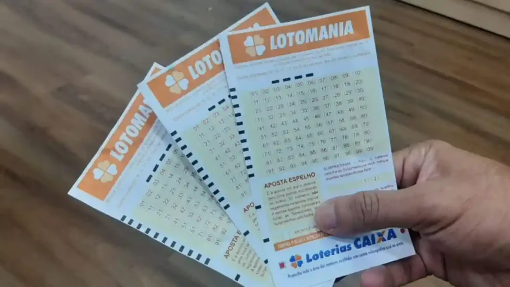Mão segurando três bilhetes da Lotomania da Caixa com números para apostar