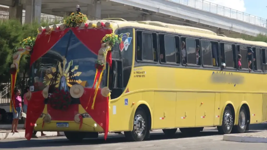 Ônibus amarelo com romeiros a caminho de Juazeiro decorado com tecido vermelho e imagem religiosa na parte frontal