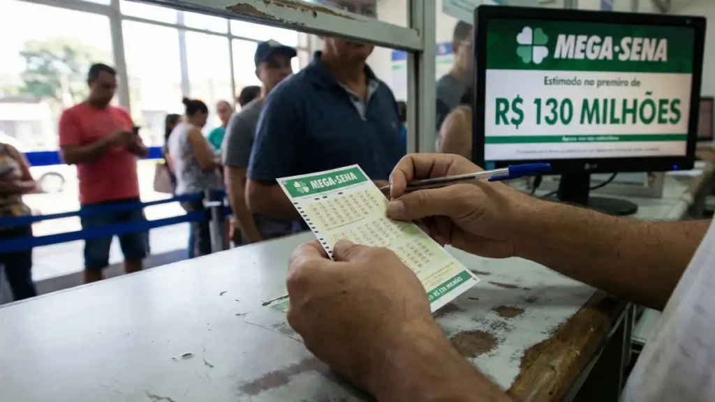 Apostador preenche bilhete da Mega-Sena no balcão de uma lotérica; ao fundo, monitor exibe “Mega-Sena” e “R$ 130 milhões”.