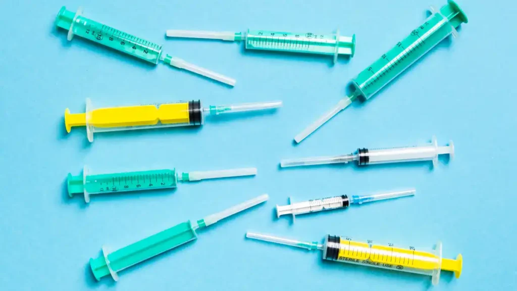 Seringas e agulhas descartáveis espalhadas sobre fundo azul, representando materiais médicos de uso único em ambiente hospitalar